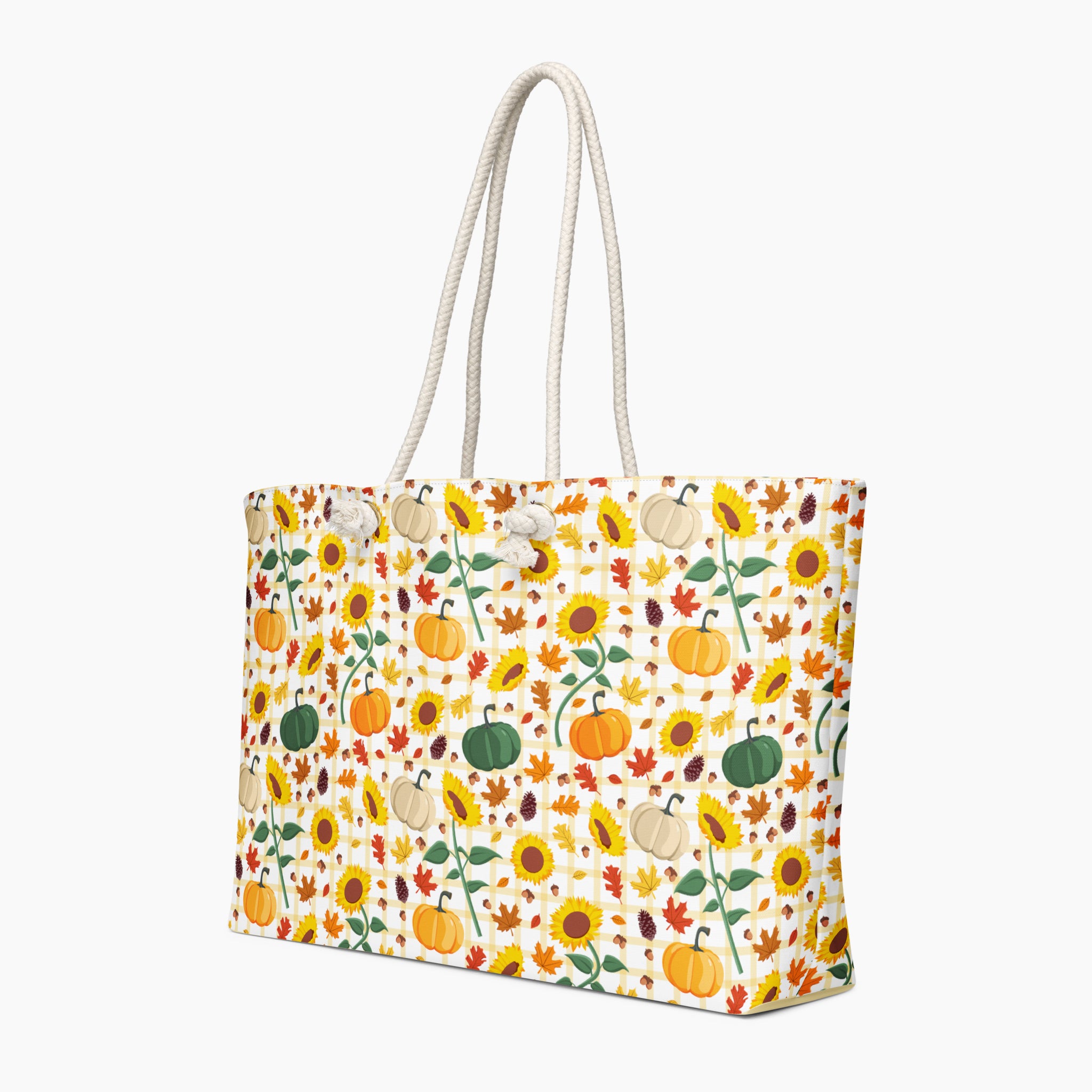 A tote bag featuring an all-over autumn pattern featuring pumpkins, sunflowers, leaves, and acorns. The bag has thick white rope handles and is shown from a three-quarters angle against a light gray studio background.