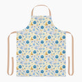 A light beige apron with a colorful repeating pattern of blue menorahs, Star of David symbols, dreidels, doves, and olive branches, shown against a plain light grey studio backdrop.