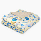 A folded blanket with a light beige sherpa lining and a printed fabric cover featuring blue and gold Star of David, Menorah, and dove motifs on a pale yellow background.