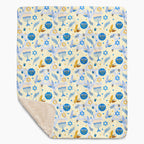 A rectangular blanket with a cream-colored sherpa lining and a printed front featuring a festive pattern of blue and gold menorahs, Star of David, dreidels, doves, and olive branches on a pale yellow background.