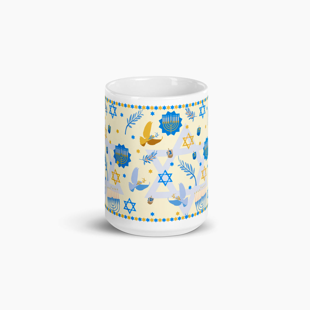 A white ceramic mug with a festive Hanukkah-themed print featuring blue Star of David, Menorahs, doves, and dreidels on a pale yellow background, set against a clean light grey studio backdrop.
