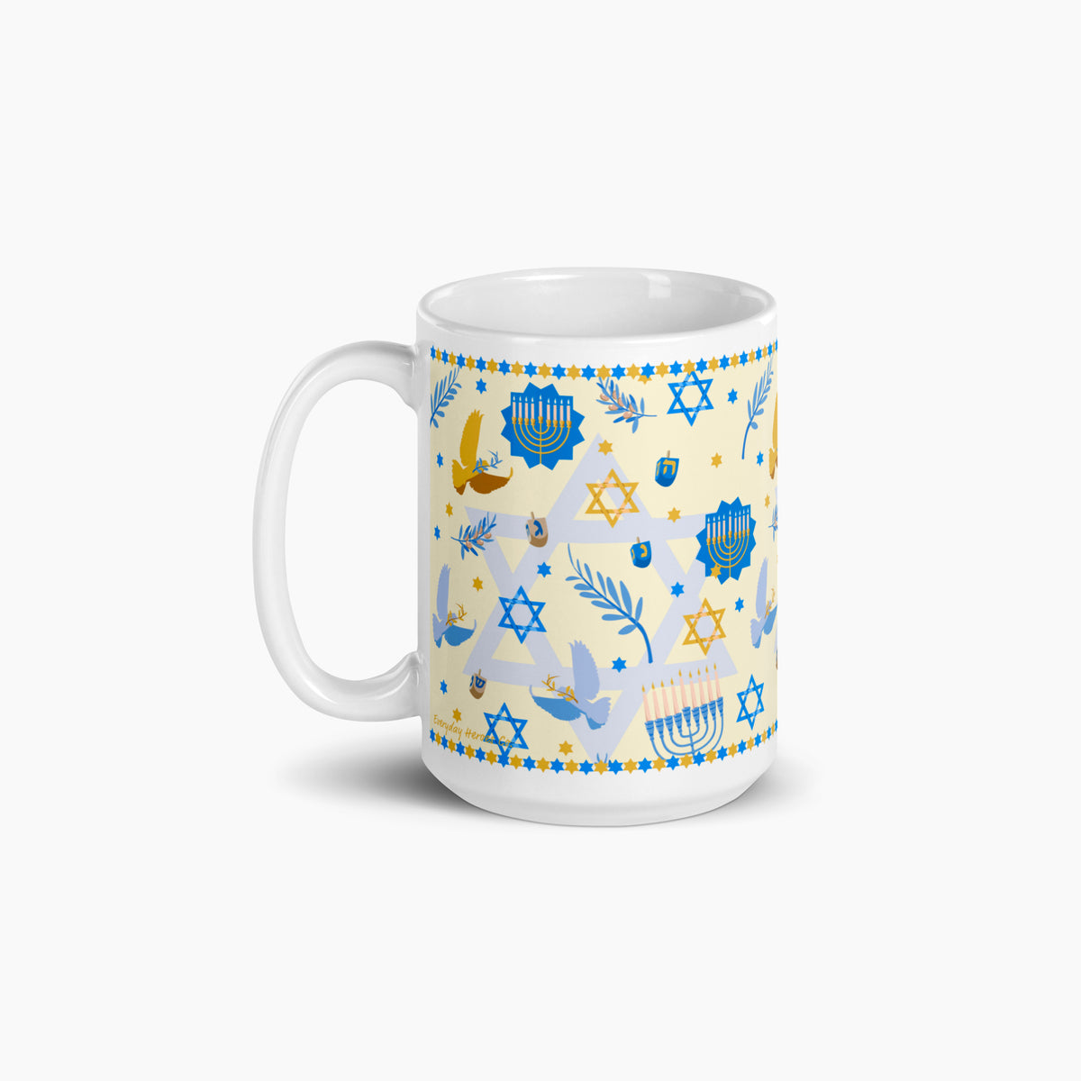 A white ceramic mug with a festive Hanukkah-themed print featuring blue Star of David, Menorahs, doves, and dreidels on a pale yellow background, set against a clean light grey studio backdrop.