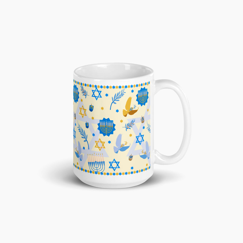 A white ceramic mug with a festive Hanukkah-themed print featuring blue and gold illustrations of menorahs, dreidels, stars, and golden and blue doves on a pale yellow background.
