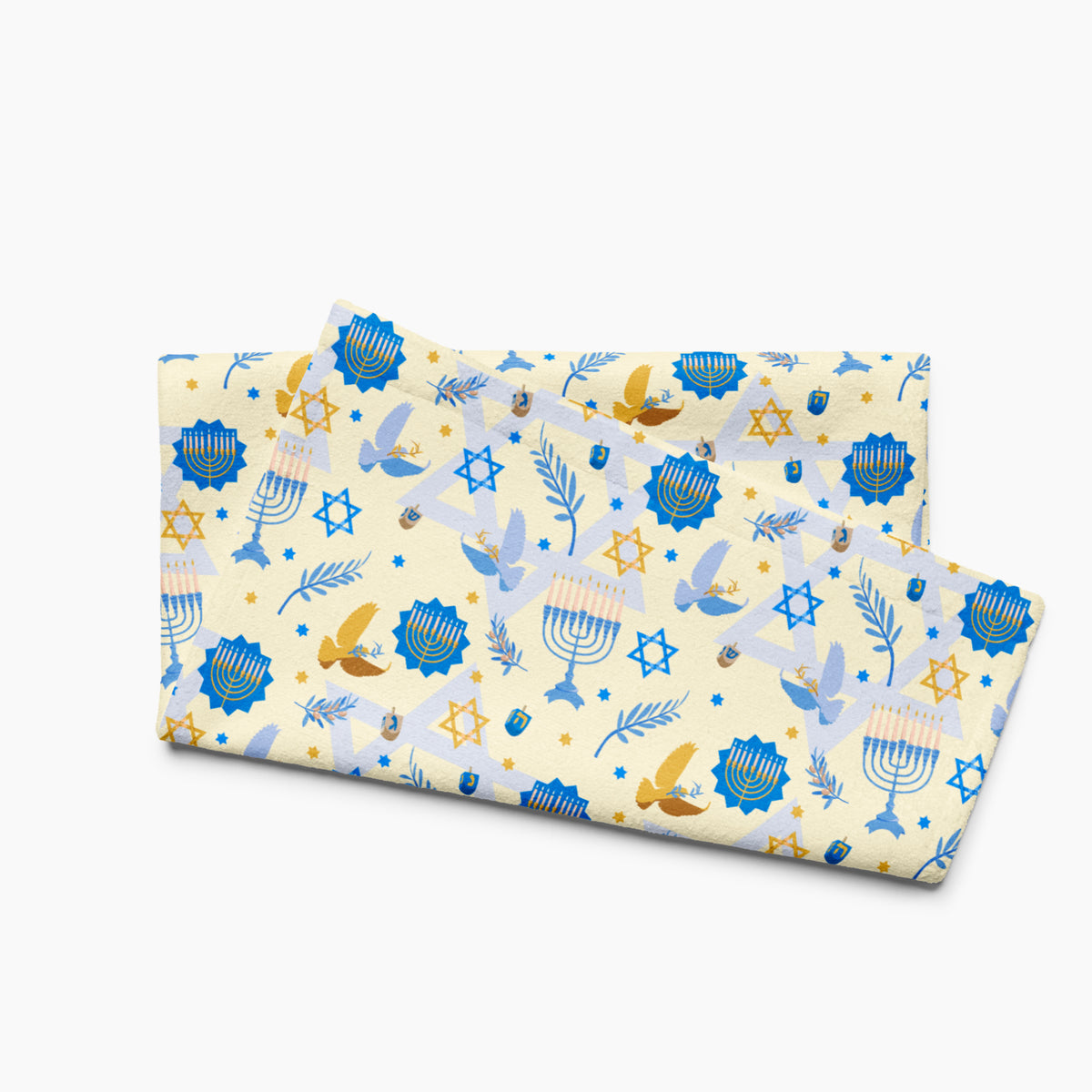 A folded microfiber fabric hand towel with a festive Hanukkah pattern on a cream background, featuring blue menorahs, Star of David motifs, dreidels, doves, and olive branches.