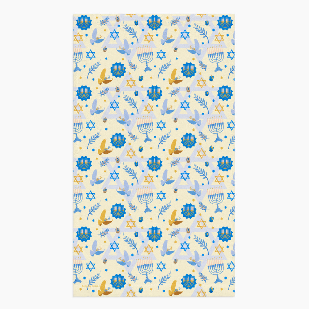 A rectangular microfiber fabric hand towel with a repeating festive pattern featuring blue menorahs, blue Star of David motifs, blue circular medallions, gold stars, and small gold and blue doves on a pale cream background.