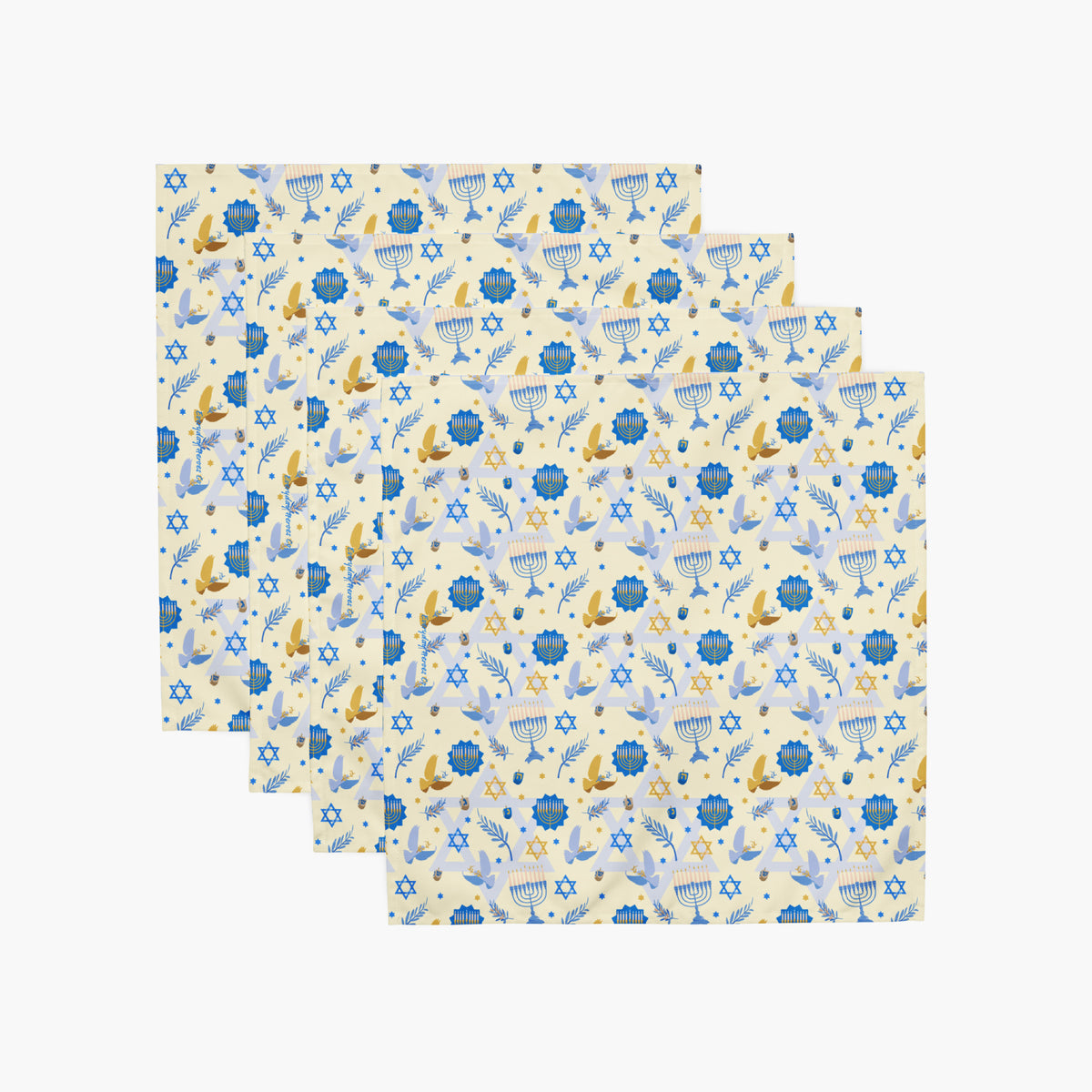 Four square cloth napkins with a festive Hanukkah-themed pattern featuring blue Star of David, dreidels, doves, olive branches, and menorahs on a pale yellow background, arranged in a staggered stack on a light gray background.