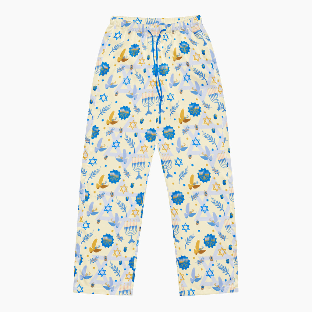 A pair of pajama pants with a festive Hanukkah holiday print featuring blue menorahs, Star of David symbols, dreidels, olive branches, and doves on a pale yellow background, complete with a blue drawstring waist.
