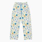 A pair of pajama pants with a festive Hanukkah holiday print featuring blue menorahs, Star of David symbols, dreidels, olive branches, and doves on a pale yellow background, complete with a blue drawstring waist.