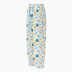 A pair of pajama pants with a festive Hanukkah holiday print featuring blue menorahs, Star of David symbols, dreidels, olive branches, and doves on a pale yellow background, complete with a blue drawstring waist shown from the side against a light grey studio backdrop.