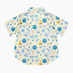The back side of a short-sleeve button-up pajama shirt with a festive Hanukkah-themed print featuring blue menorahs, Star of David emblems, lulav and olive branches and gold and blue doves on a pale yellow background.