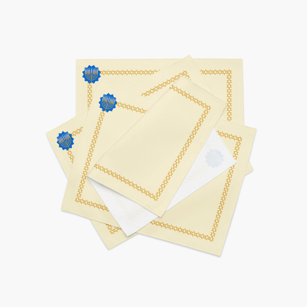 A stack of 4 rectangular cream-colored fabric placemat with a decorative border. The border features a repeating gold Star of David pattern around the edges, and a blue medallion with a gold menorah design in the top-left corner.
