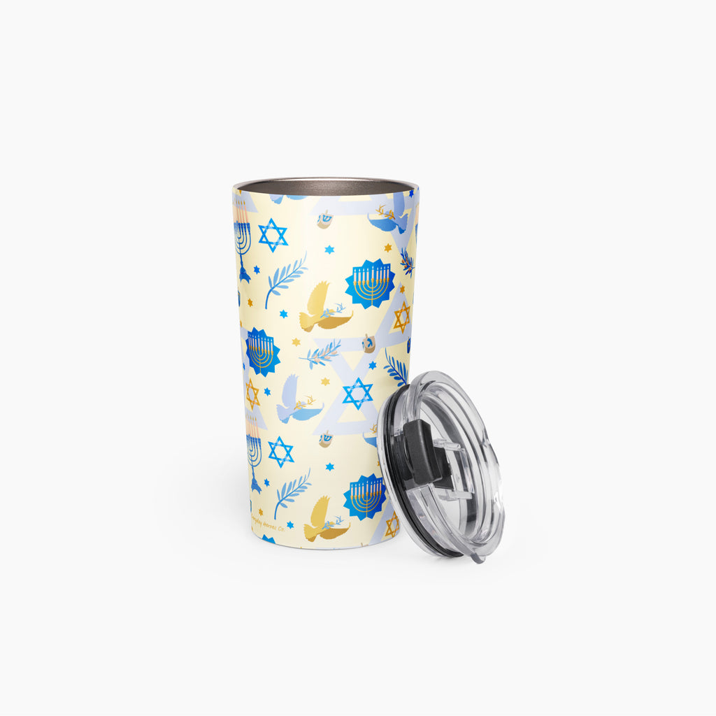 A stainless steel travel tumbler with a light cream background and a blue and gold Hanukkah-themed pattern, shown with its clear lid leaning against it on a white background.