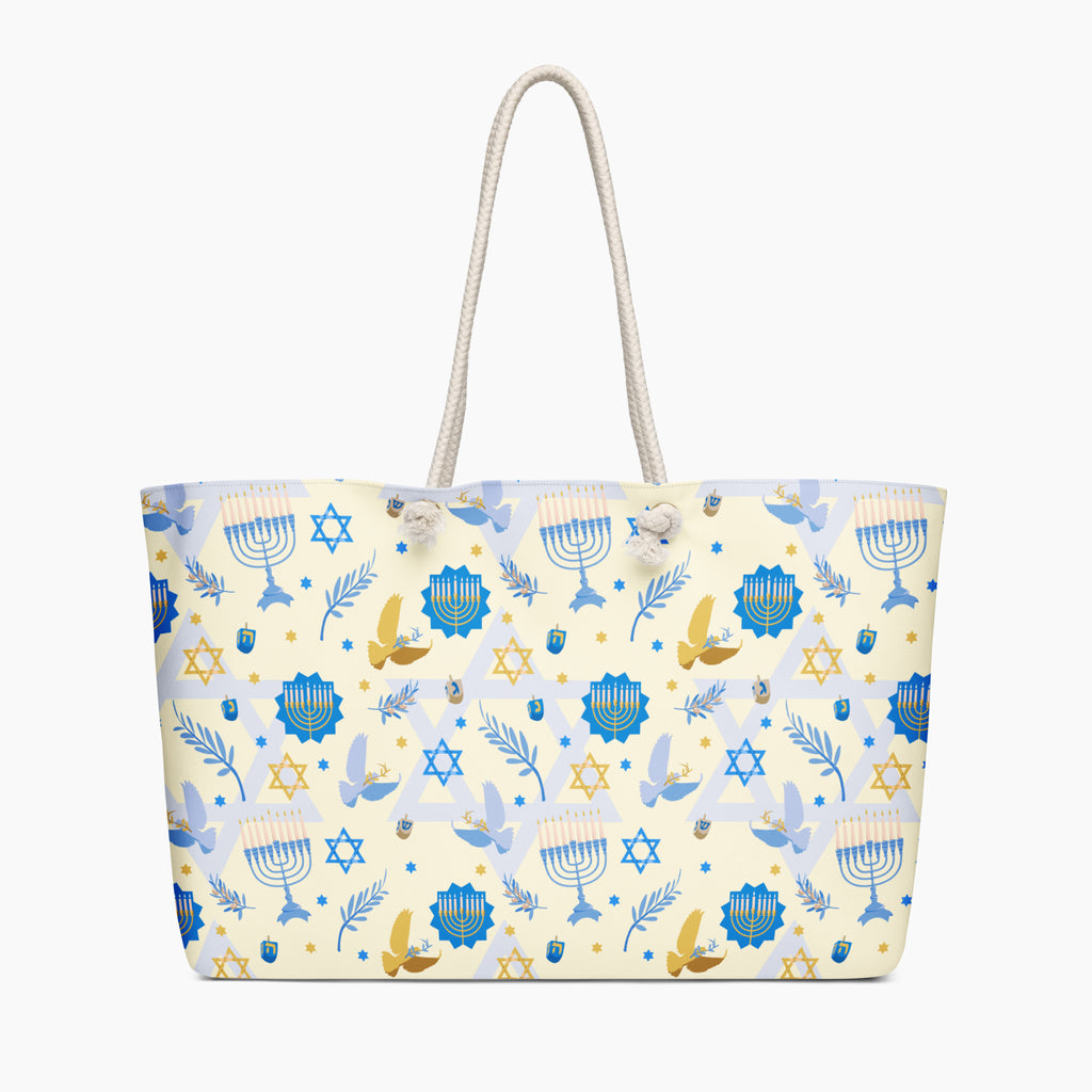 A cream-colored tote bag with a festive Jewish-themed pattern featuring blue menorahs, Star of David emblems, blue and gold doves on a light cream background, complete with two cream rope handles.