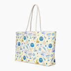 A tote bag with a festive Hanukkah pattern featuring blue menorahs, Star of David, dreidels, and gold and blue doves on a cream background, complete with two thick white rope handles.