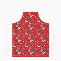 A red apron with a festive Christmas pattern featuring white reindeer, green Christmas trees, snowflakes, gift boxes and candy canes, shown against a plain light grey studio background.