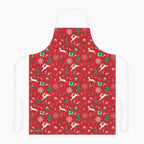 A red apron with a festive Christmas pattern featuring white reindeer, green Christmas trees, snowflakes, gift boxes and candy canes, shown against a plain light grey studio background.