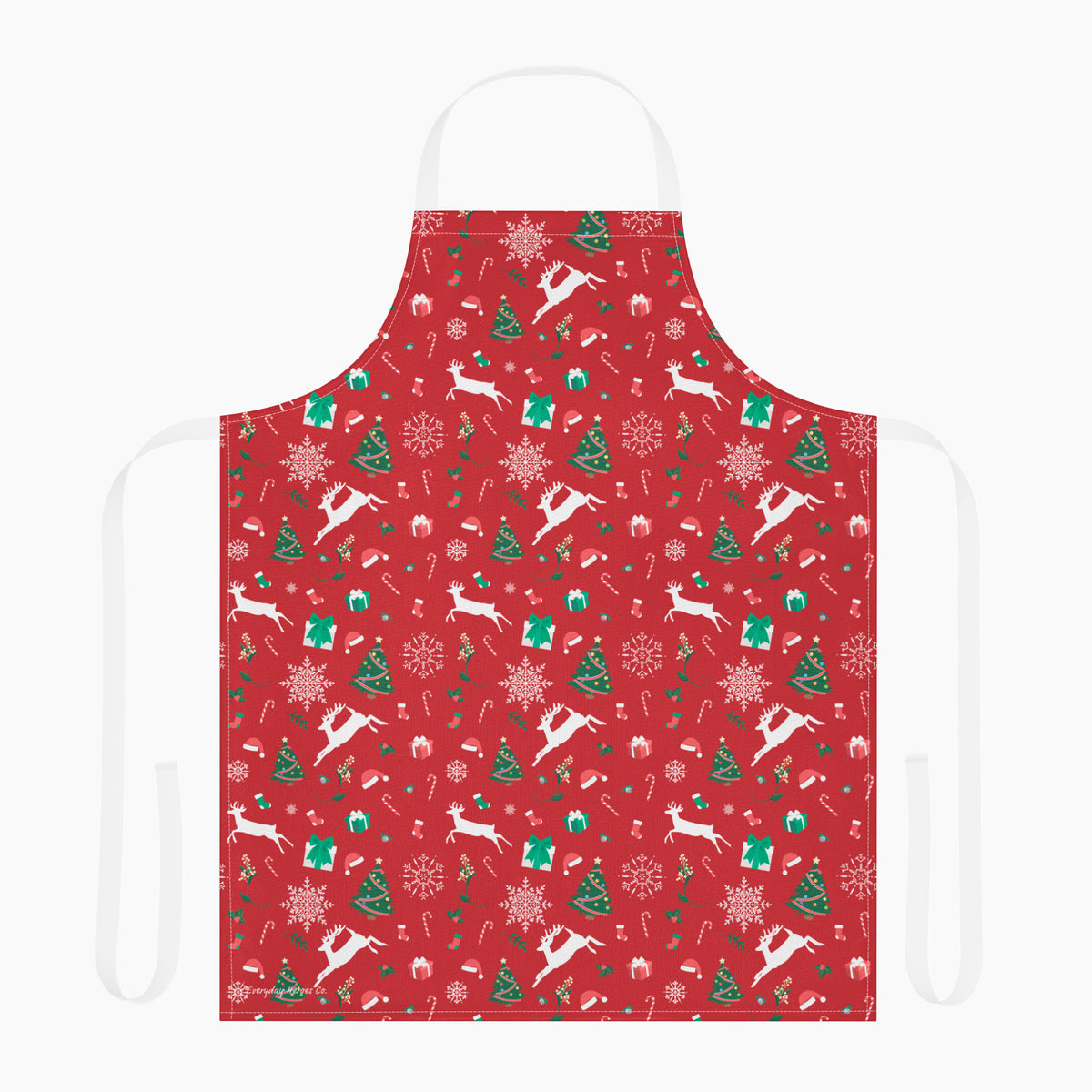 A red apron with a festive Christmas pattern featuring white reindeer, green Christmas trees, snowflakes, gift boxes and candy canes, shown against a plain light grey studio background.