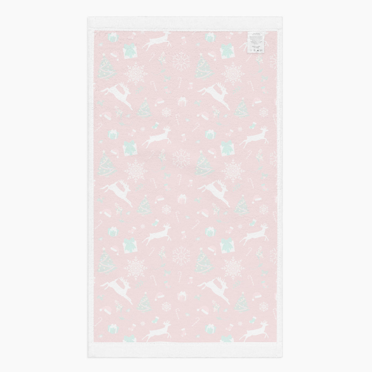 The white backing of a rectangular red holiday-themed patterned microfiber fabric hand towel featuring white reindeer, green Christmas trees, snowflakes, candy canes, and gift boxes, shown on a light gray background.