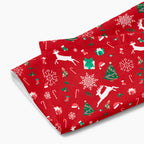 A folded rectangular red holiday-themed patterned microfiber fabric hand towel featuring white reindeer, green Christmas trees, snowflakes, candy canes, and gift boxes, shown on a light gray background.