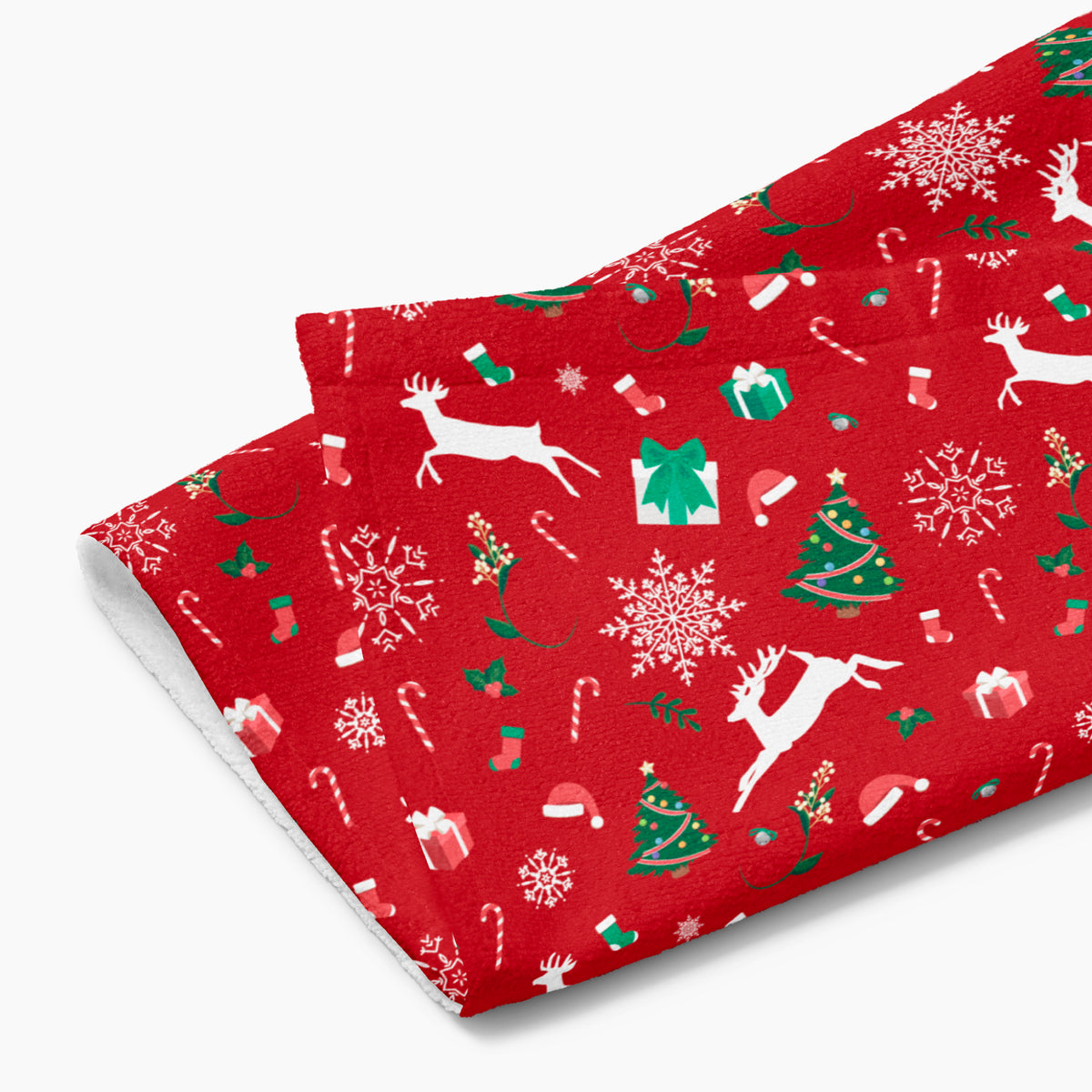 A folded rectangular red holiday-themed patterned microfiber fabric hand towel featuring white reindeer, green Christmas trees, snowflakes, candy canes, and gift boxes, shown on a light gray background.