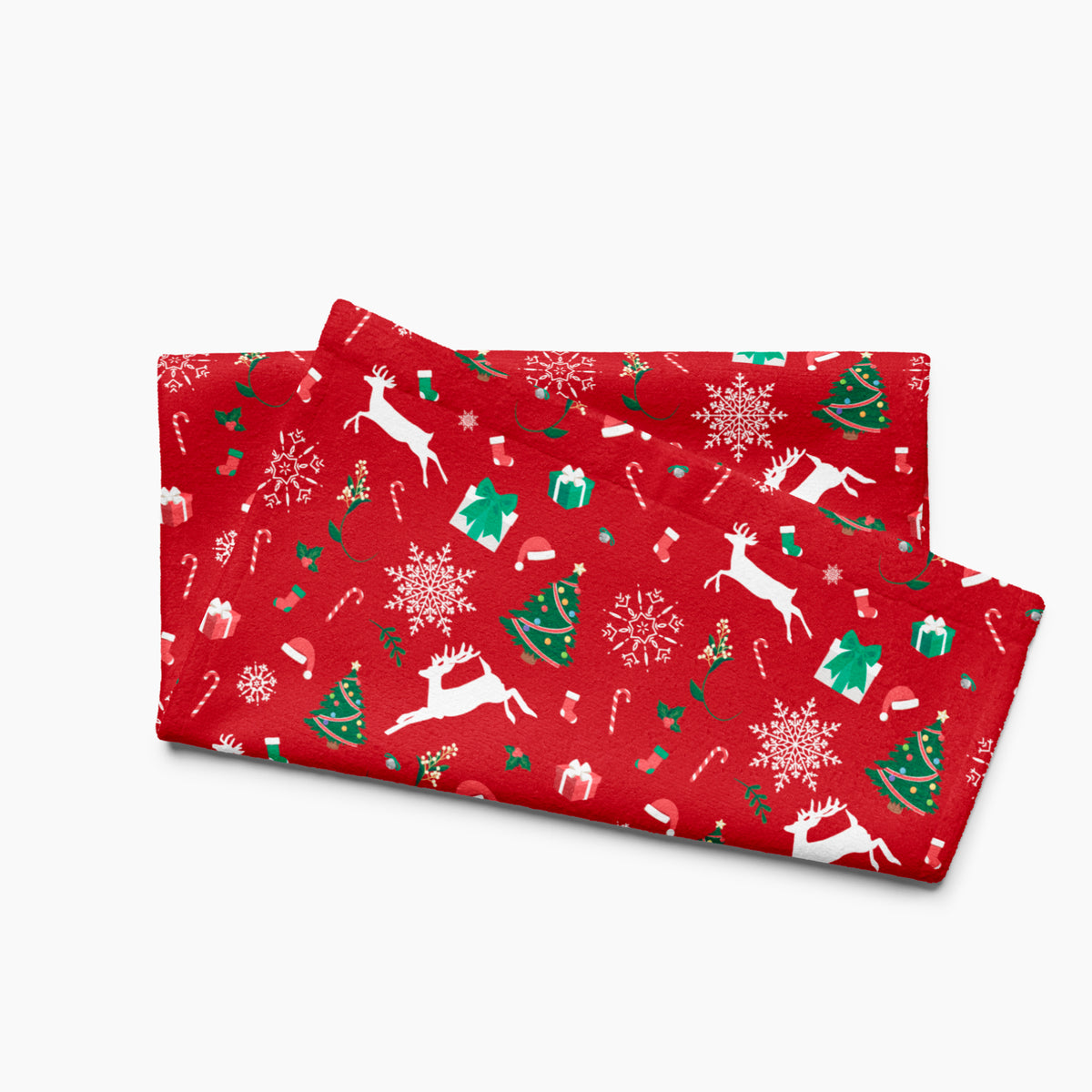 A folded red holiday-themed patterned microfiber fabric hand towel featuring white reindeer, green Christmas trees, snowflakes, candy canes, and gift boxes, shown on a light gray background.