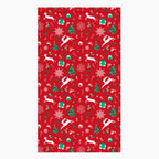 A rectangular red holiday-themed patterned microfiber fabric hand towel featuring white reindeer, green Christmas trees, snowflakes, candy canes, and gift boxes, shown on a light gray background.