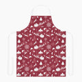 A deep red apron with a white winter holiday pattern featuring snowflakes, Christmas trees, reindeer, sleighs, and mountains, shown against a plain light grey background.