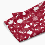 A folded deep red hand towel featuring a repeating white Christmas pattern with Santa Claus, sleighs, trees, snowflakes, and winter motifs, shown on a light gray background.