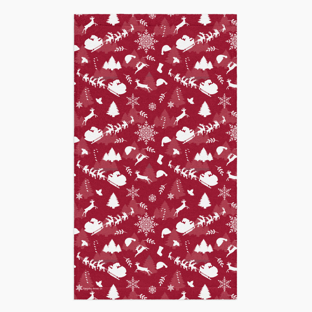 A rectangular deep red hand towel featuring a repeating white Christmas pattern with Santa Claus, sleighs, trees, snowflakes, and winter motifs, shown on a light gray background.