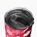 Close-up of a deep red insulated tumbler with a clear lid and black flip cover, decorated with white holiday snowflakes and silhouettes, on a light gray background.