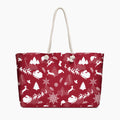 A deep red tote bag with a white Christmas-themed pattern featuring Santa Claus, reindeer, snowflakes, and trees, complete with two cream rope handles.