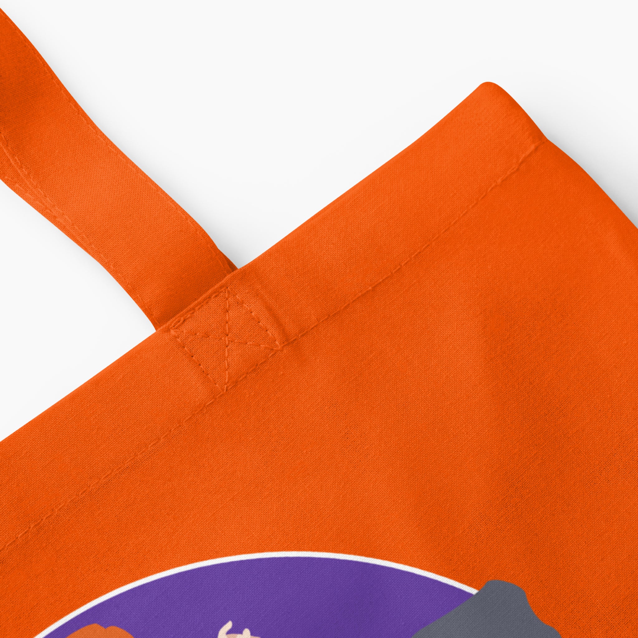 Close-up of an orange canvas tote bag with a purple circular graphic on a light grey background.