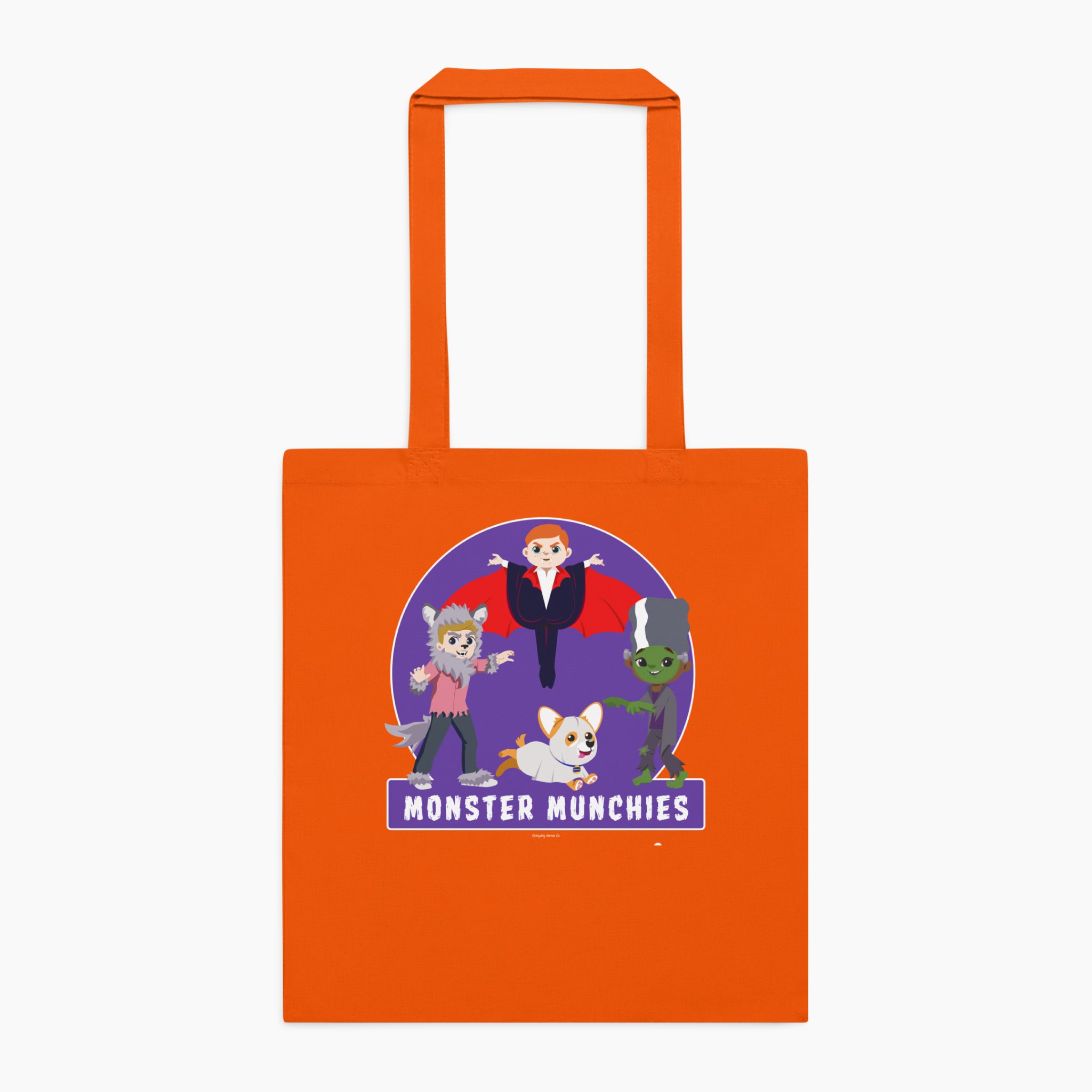 An orange canvas tote bag with orange handles, featuring a colorful graphic print of cartoon monster characters over a purple circle with the text 'MONSTER MUNCHIES' on the front, set against a plain light grey background.