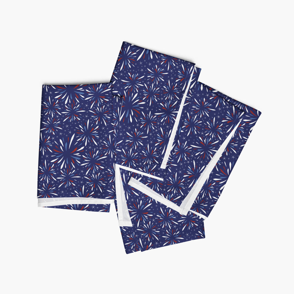 Four folded cloth napkins with a colorful pattern of firework-themed illustrations on a white background.