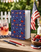Notebook with custom printed patriotic design on a wooden table with American flag and fruit bowl.