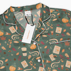 A close-up of a pajama top with a sage green base and an all-over pumpkin spice-themed print featuring coffee cups, pumpkins, leaves, and fall spices. The pajama has white piping along the collar, placket, and pocket, and is shown with a white brand tag and paper labels attached.
