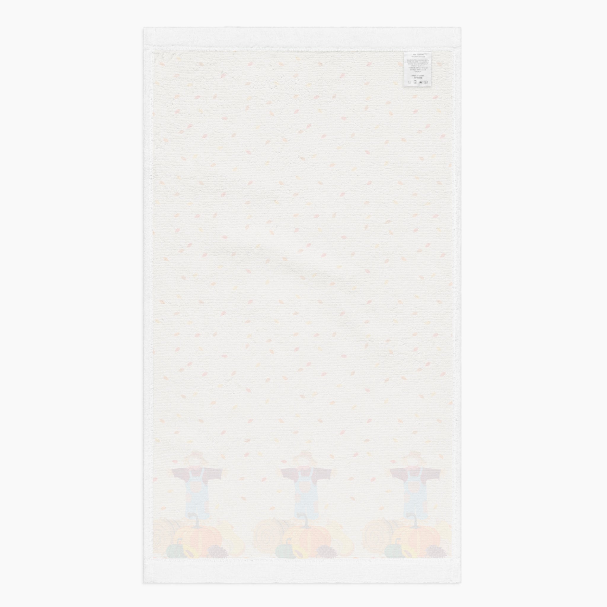 A white backside of a rectangular beige kitchen towel, featuring an all-over autumn leaf print and a row of three scarecrows with pumpkins and gourds along the bottom edge.