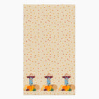 A rectangular beige kitchen towel, featuring an all-over autumn leaf print and a row of three scarecrows with pumpkins and gourds along the bottom edge.