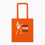 An orange canvas tote bag with two top handles, featuring a white graphic of a skeleton playing an electric guitar next to the text 'BONE TO BE WILD' in white and black lettering staged flat against a light grey background.