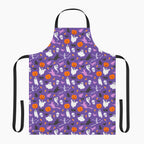 A purple apron with a black neck loop and waist ties, featuring an all-over Halloween pattern of orange pumpkins, white ghosts, black cats, and witches on a light gray background.