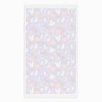 The white back of a rectangular cloth kitchen towel featuring a repeating Halloween pattern on a purple background, with white ghosts, black cats, orange pumpkins, and small candy corns.
