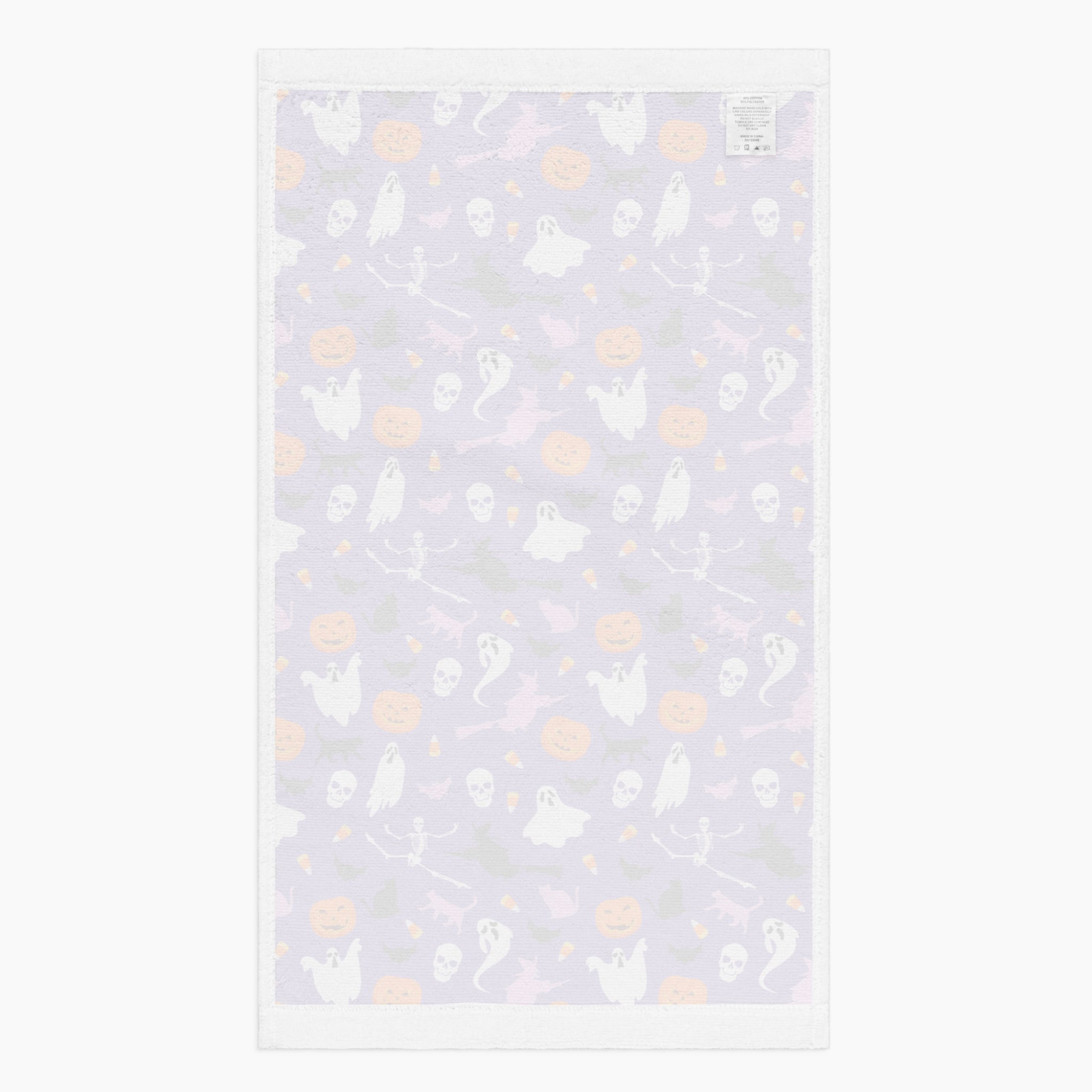 The white back of a rectangular cloth kitchen towel featuring a repeating Halloween pattern on a purple background, with white ghosts, black cats, orange pumpkins, and small candy corns.