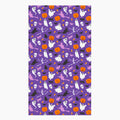A rectangular cloth kitchen towel featuring a repeating Halloween pattern on a purple background, with white ghosts, black cats, orange pumpkins, and small candy corns.