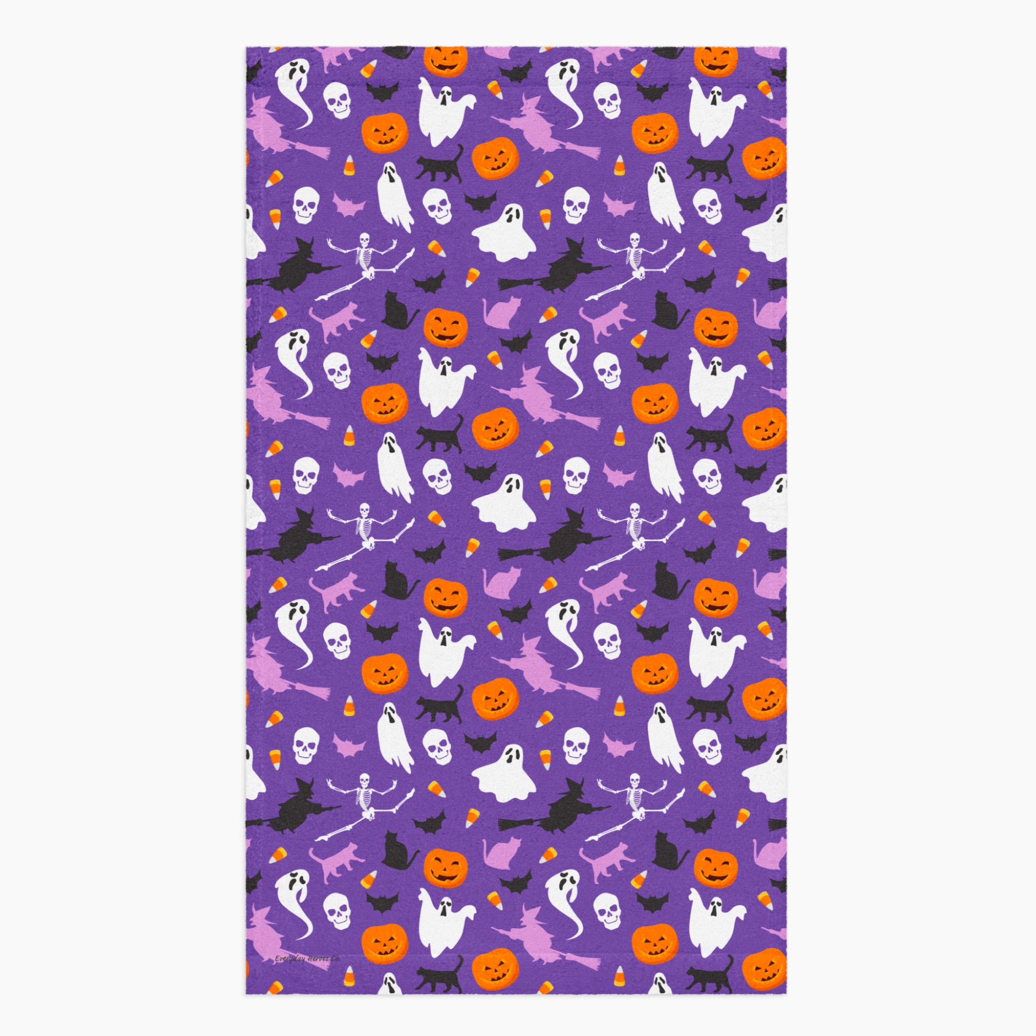A rectangular cloth kitchen towel featuring a repeating Halloween pattern on a purple background, with white ghosts, black cats, orange pumpkins, and small candy corns.