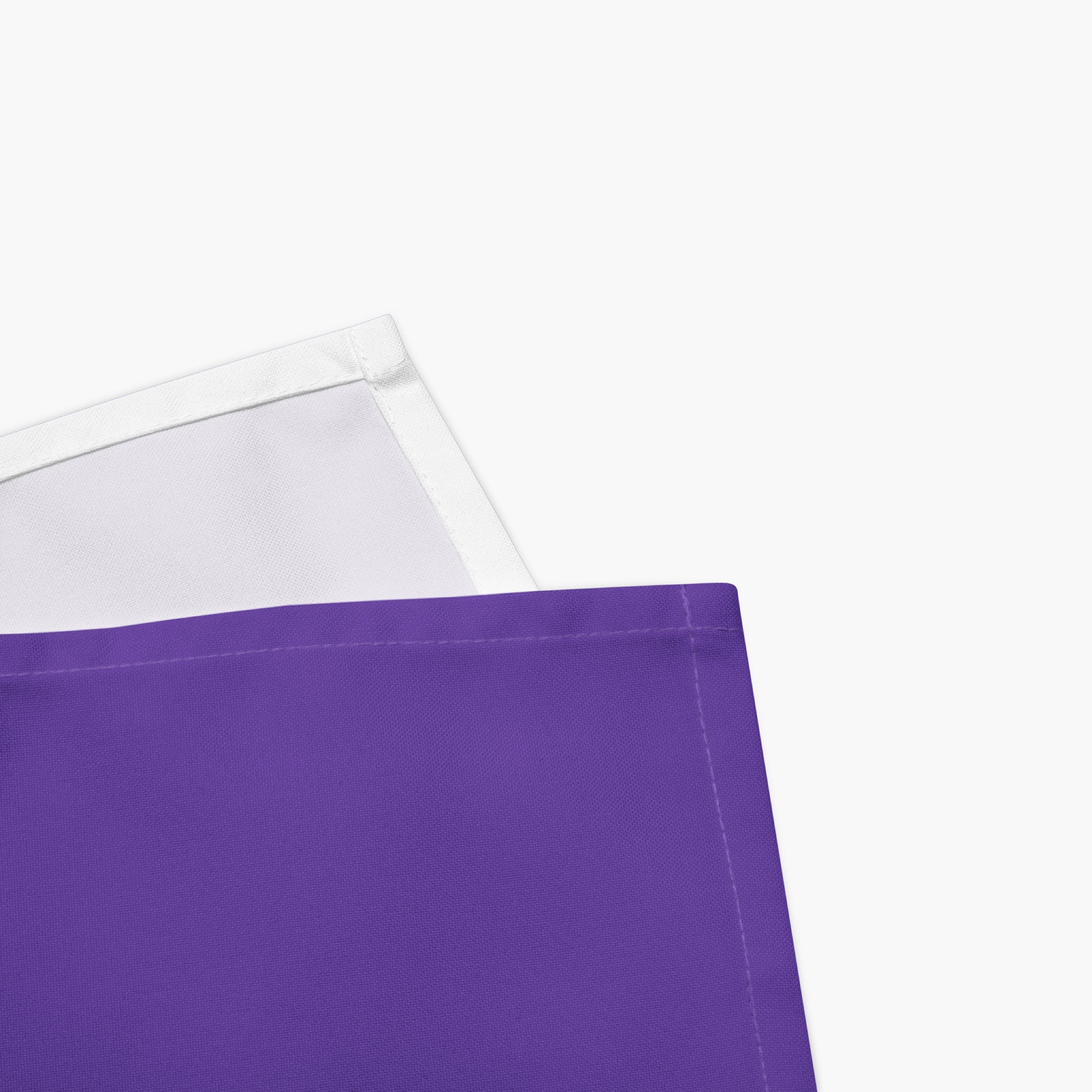 A close-up of a purple cloth napkin showing its solid purple front and a white reverse side with a stitched edge, set against a plain light-grey background.