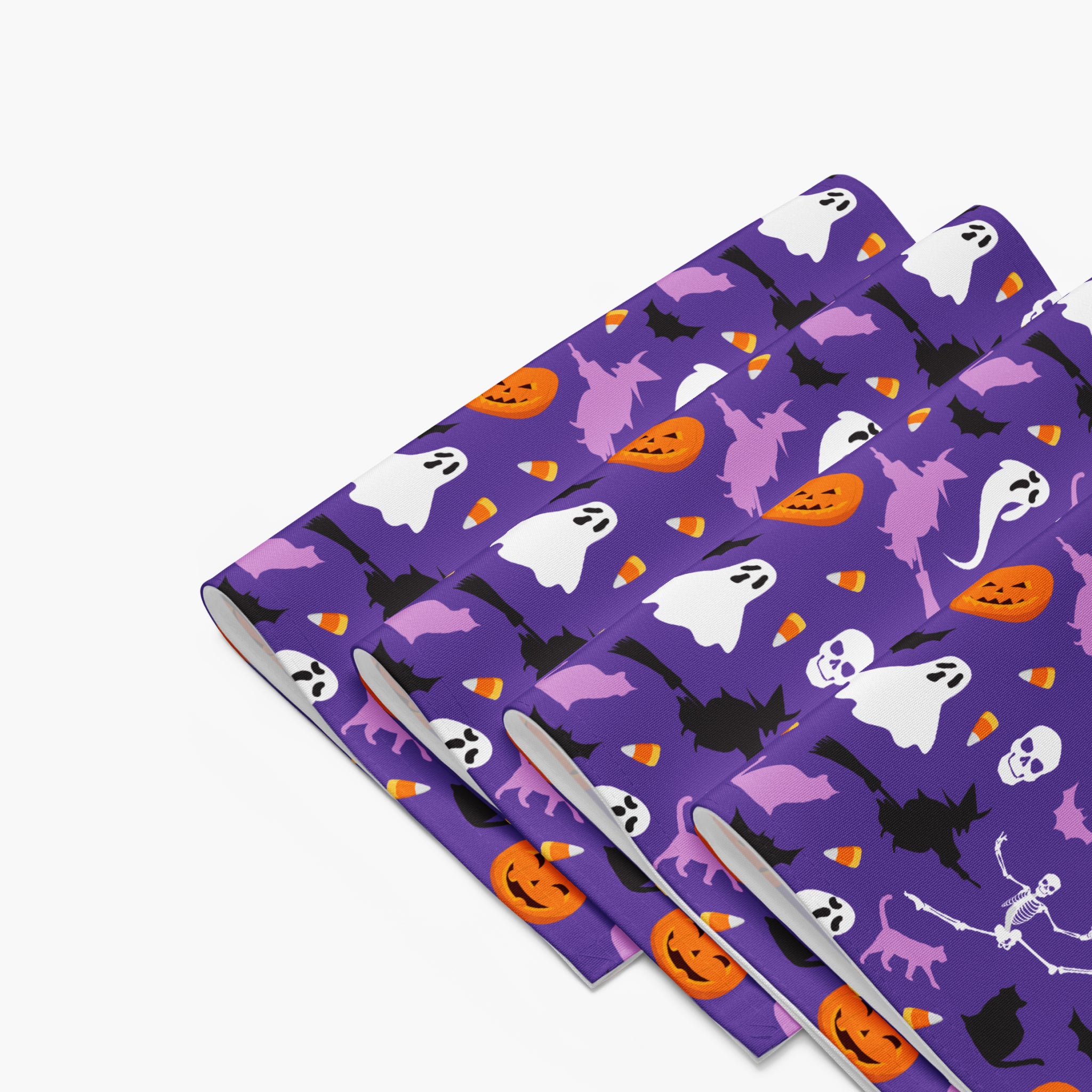 Purple Halloween-themed cloth placemats folded with a repeating pattern of white ghosts, orange pumpkins, black bats, and purple witches, shown on a light gray background.