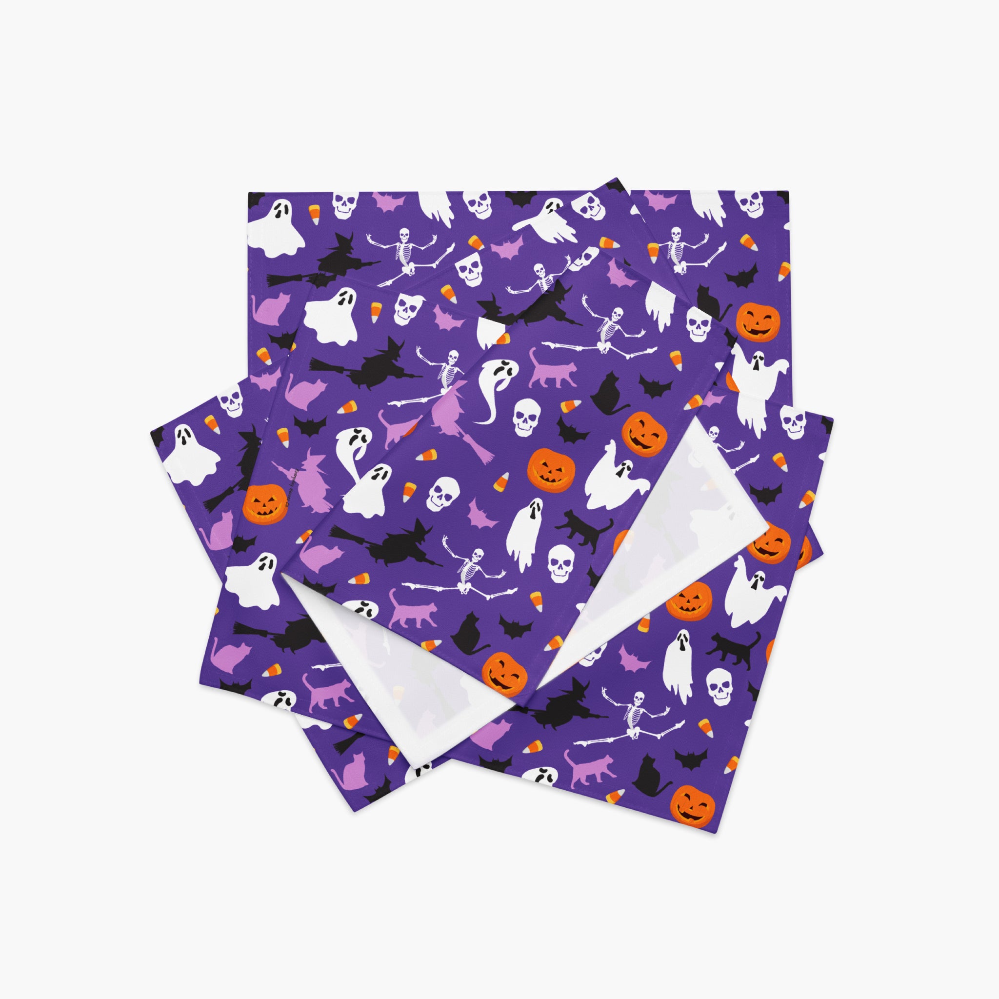 A stack of square Halloween-themed placemats featuring a purple background with a repeating pattern of white ghosts, black bats, skeletons, orange pumpkins, and witches, with a white reverse side.