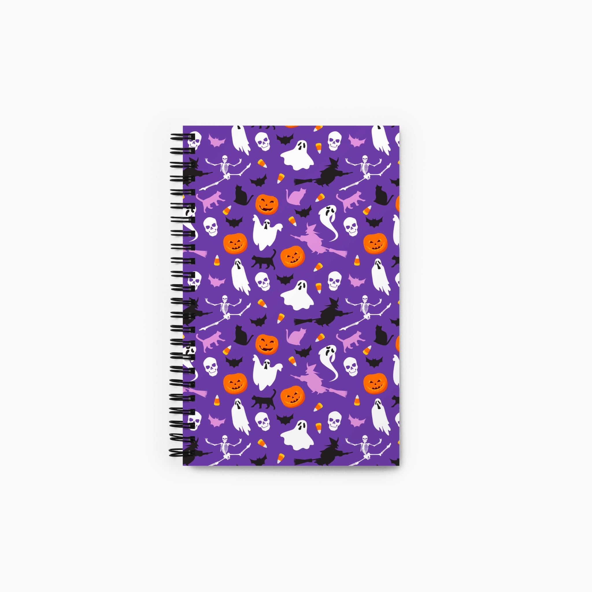 A spiral-bound notebook with a purple cover decorated with a repeating Halloween pattern of ghosts, pumpkins, bats, skulls, and witches, shown on a light gray background.