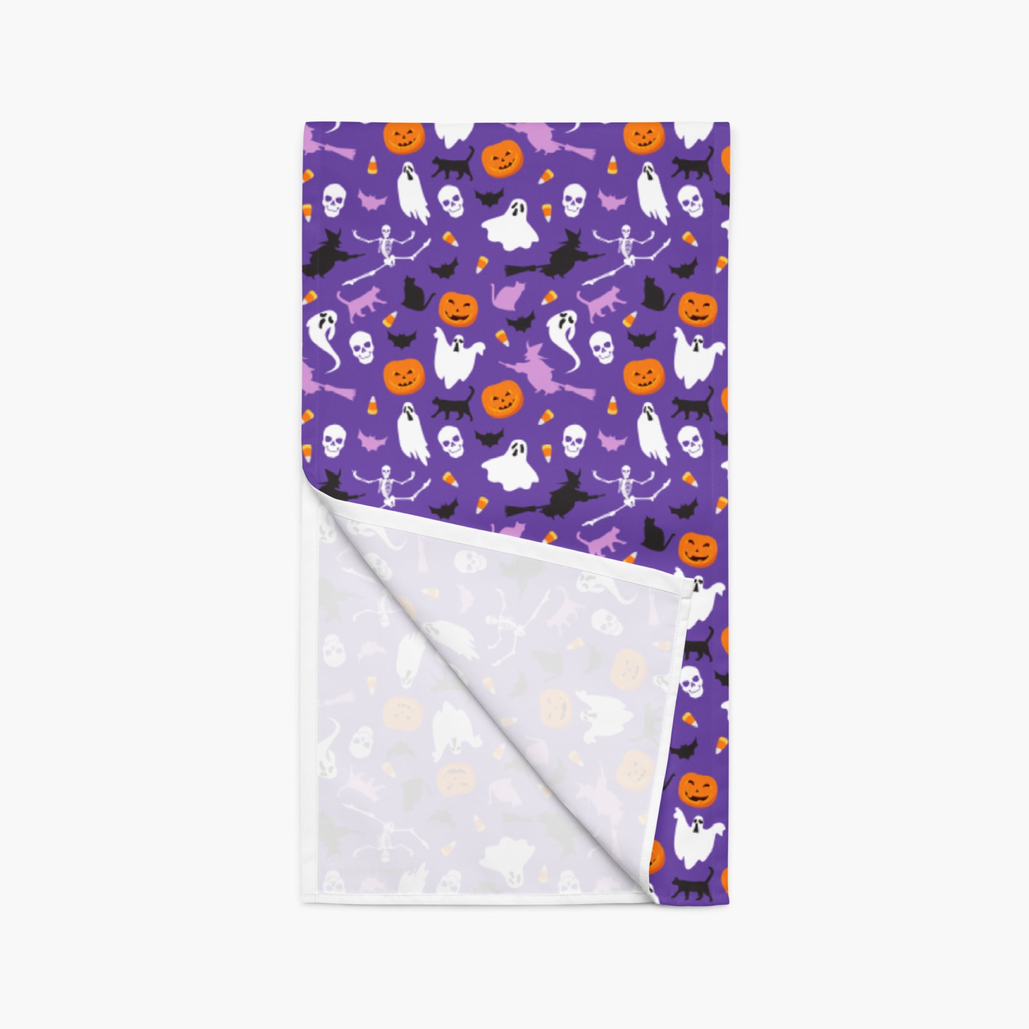 A folded table runner with a purple Halloween pattern on one side and a white reverse side, displayed on a light gray background.
