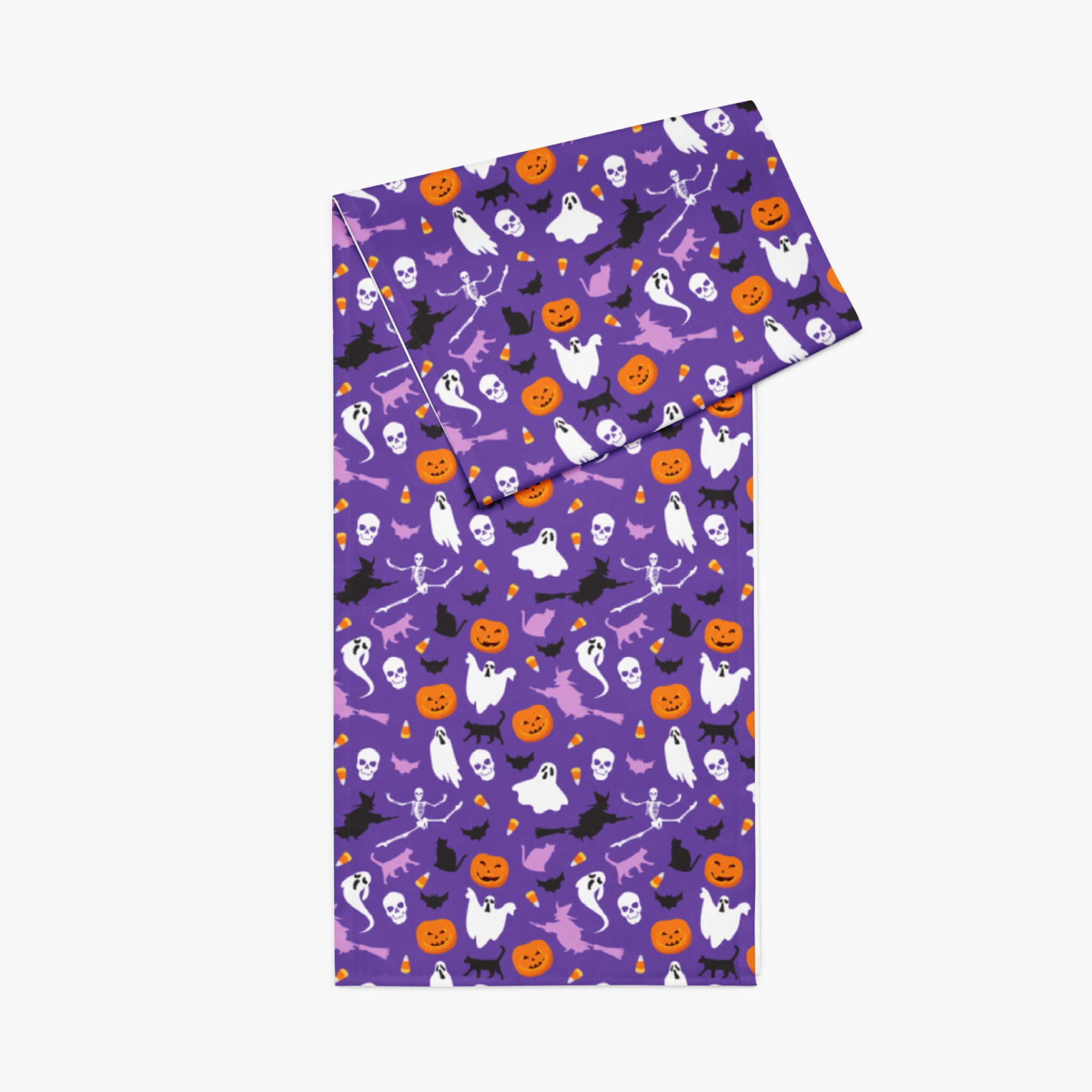A rectangular fabric table runner featuring a vibrant purple Halloween pattern with cartoon ghosts, pumpkins, bats, and witches, shown on a light gray background.